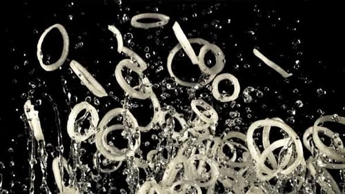 A Pile of Sliced Onion Rings with Drops of Water Soars Up and Falls Down