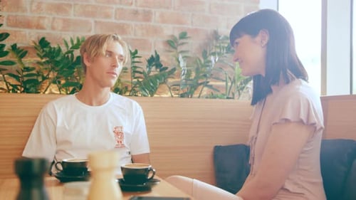 Two Friends Talking and Drinking Coffee at a Booth in Interior Cafe