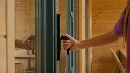 A close-up of a woman's hand grasping the doorknob and opening the glass door to the house