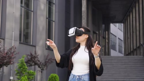 Asian woman working on virtual screen in augmented reality glasses near modern office building