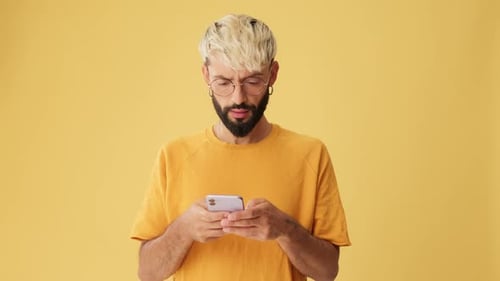 Man with phone in his hands is surprised, wow, isolated on yellow background in studio