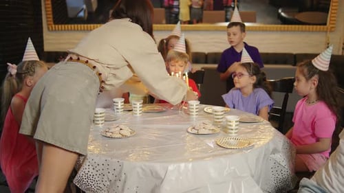A mãe do aniversariante traz e coloca um bolo de aniversário com velas na mesa