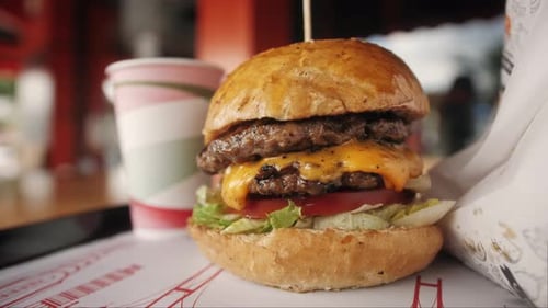 Großer Burger mit Rinderschnitzel, Tomaten und Gurken mit geschmolzenem Käse, Pommes frites und Getränken auf