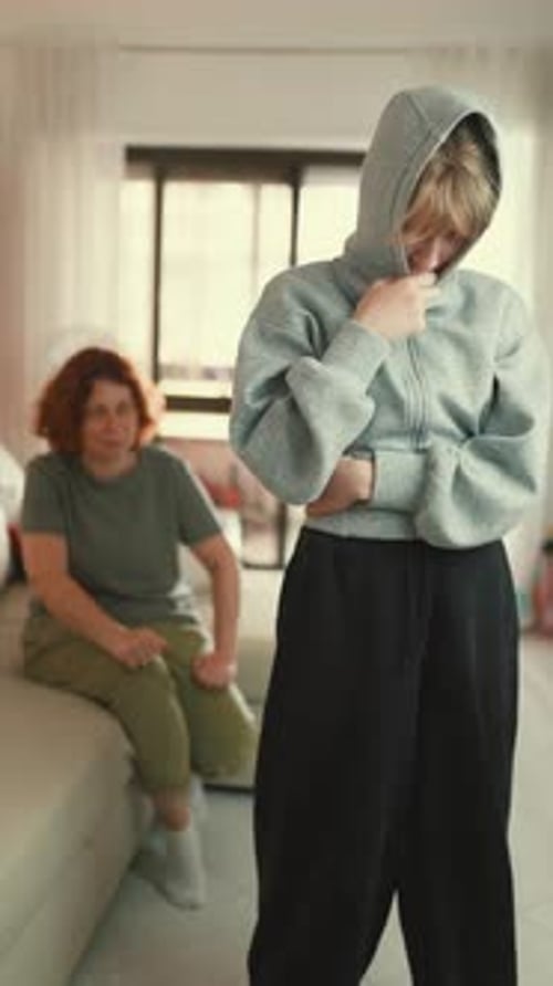 Teen Girl Stands with Hoodie Over Head While Woman Sits