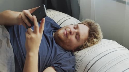Young Adult Lying in Bed Using Phone