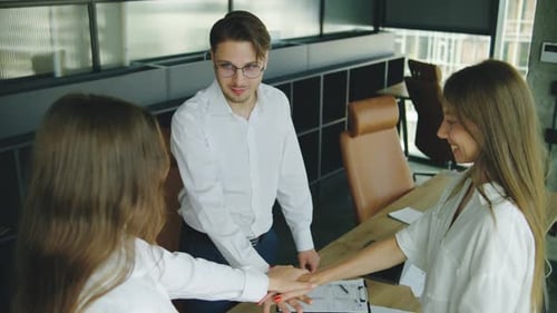 Three Coworkers Engage in a Teamwork Exercise By Placing Their Hands Together in a Modern Office
