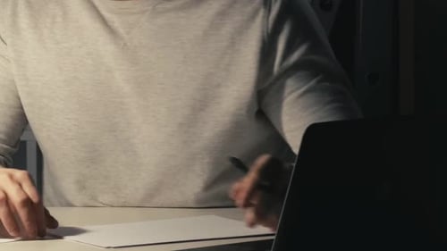 Young Man Working at Night on Laptop and Writing