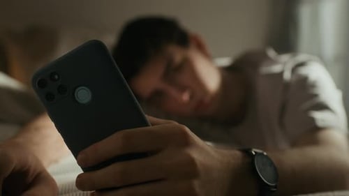 Upset Gen Z Man Doomscrolling on Smartphone in Bed