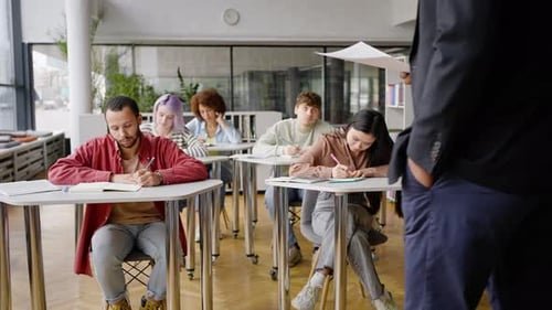 Teenage Students Pass Examination While a Teacher Walking Along the Class with Papers in His Hands