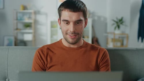 Man Smiles Using Laptop on Sofa at Home