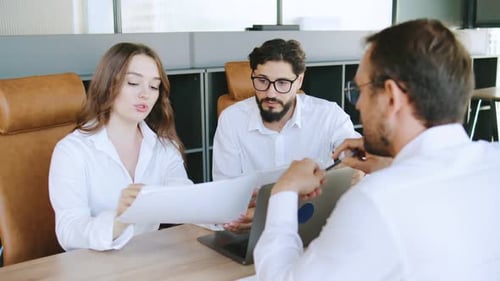 Business Meeting in Modern Office Discussing Project Details with Documents and Laptops Present