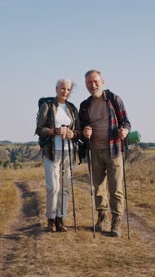 Senior Friends Hikers with Poles Stand on Road in Autumn Field