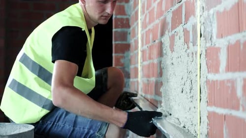 Construction Worker Applies Cement to a Brick Wall