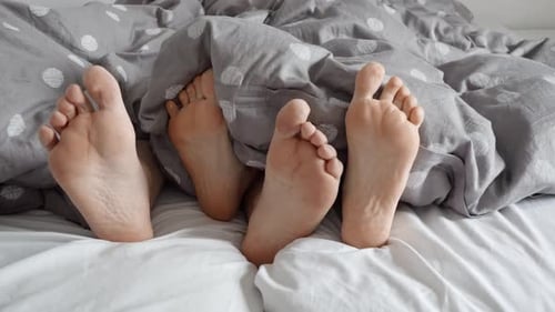 Feet Interacting Under Covers on Bed