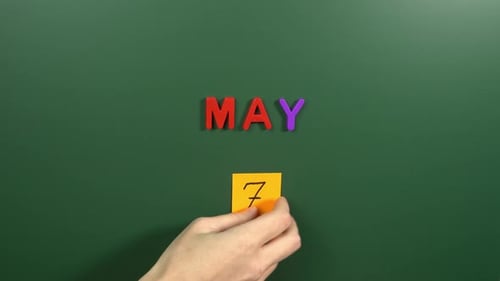 Hand sticking a sticker 7 May calendar day on school board. 7 date of May. Seventh day May. 7th