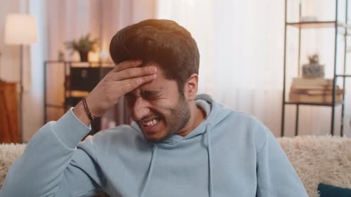 Man Rubbing Head in Frustration on Couch