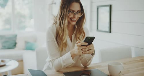 Mujer sonriendo en la oficina mientras lee un mensaje telefónico, mostrando felicidad y un lugar de trabajo moderno