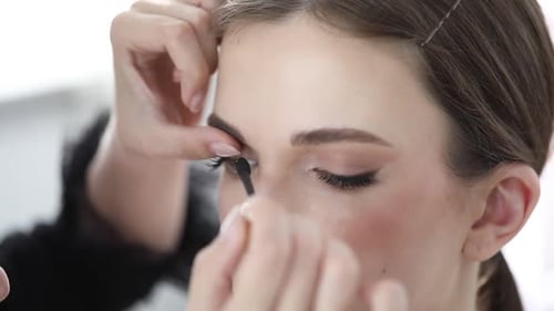 Visagist trägt Mascara auf das Gesicht einer Frau im Haus auf, Nahaufnahme