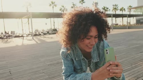 Smiling girl taking a photo on a mobile phone while standing on the street