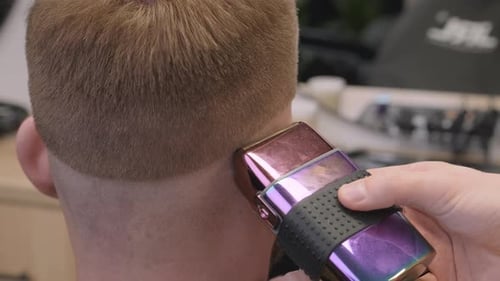 Friseur entfernt Haare hinter dem Ohr des Kunden mit einem Rasierapparat