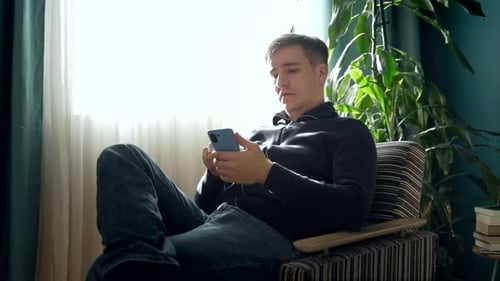 Man Using Smartphone Relaxing in Armchair at Home