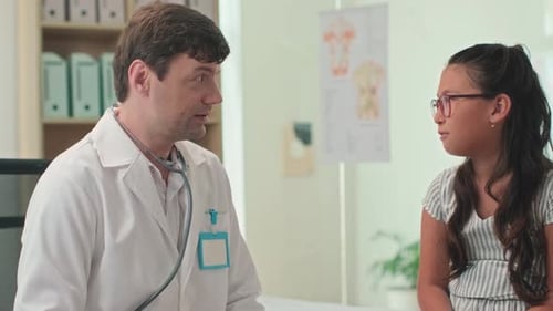 Positive Pediatrician Talking to Girl at Clinic during Appointment
