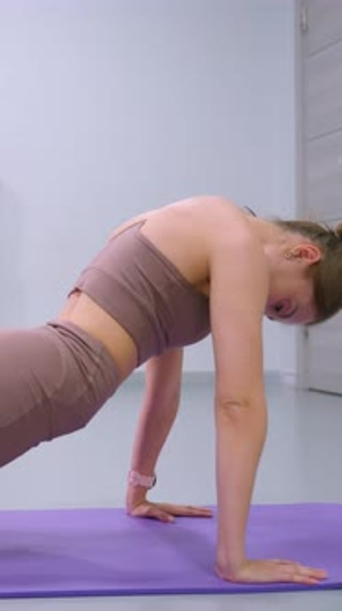 Side View of Woman Engaging in Deep Stretch on Purple Mat in Modern Gym