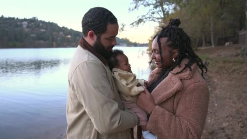 Happy Diverse Family Walking By Lake with Baby in Stroller During Autumn Day