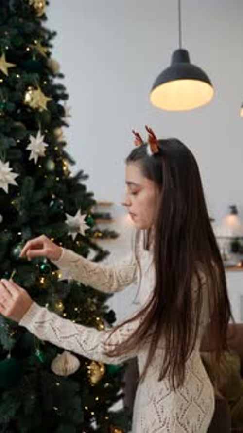 A Young Woman is Joyfully Decorating a Beautiful Christmas Tree in a Cozy Home Environment