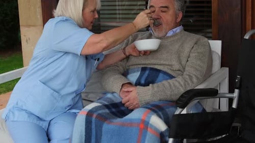Adult Caregiver Feeds Senior with Spoon Outdoors