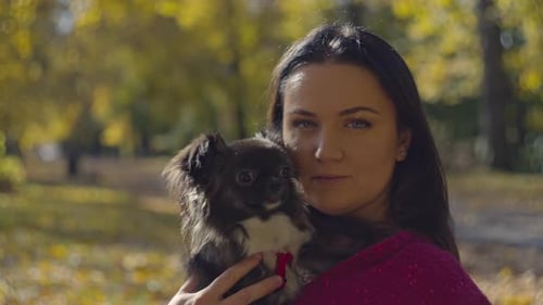 Woman Cuddling Small Dog in Autumn Park