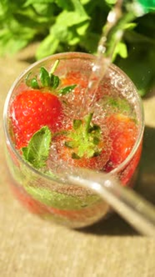 Top View Vertically Pour an Invigorating Sparkling Drink Containing Fresh Strawberries and