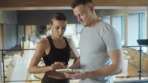 Gym Trainer Using Tablet and Speaking with Woman