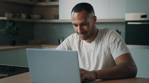 Man Smiling Working on Laptop in Kitchen