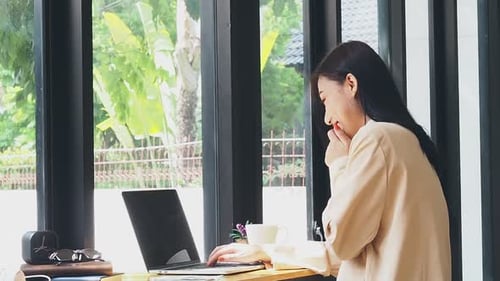 Woman Working on Laptop at Desk by Window