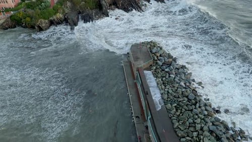 Huge foamy sea wave breaking on stony pier before flowing into harbor.