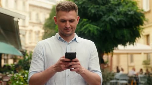 Man Using Phone on City Street in Daytime