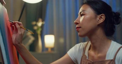 Asia lady wear apron holding palette use brush painting on canvas create artwork cozy workshop.