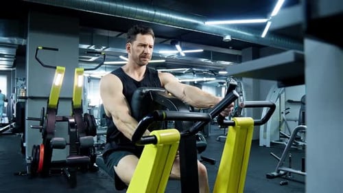 Sporty Man Training on Rowing Machine in Modern Gym Weigh Lifting Exercise