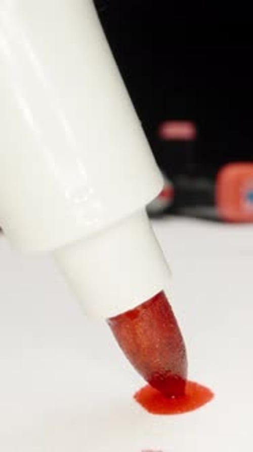 Multi-colored markers on the table. The red marker touches the paper and leaves a large smudge. extr