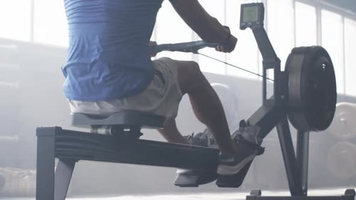 Man exercising on rowing machine in gym, focusing on fitness training