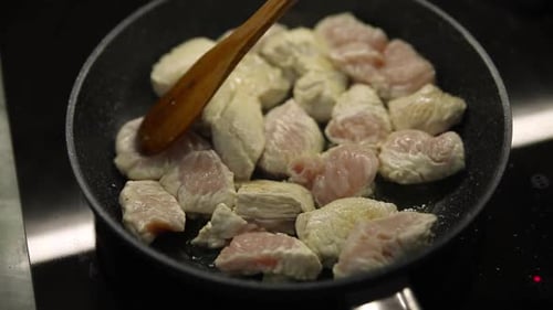 Chicken Pieces Cooking in Pan with Wooden Spatula
