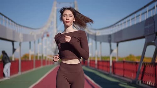 A Woman Jogs on a Bridge in Sporty Attire Showcasing Her Fitness and Strength in an Urban Setting