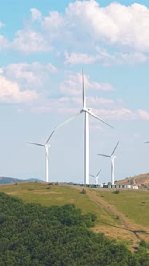 Vertical View of Wind Turbine Head and Spinning Blades Against Puffy Cloud Sky