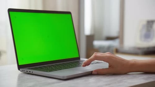 Hand Operating Laptop with Green Screen in Modern Interior