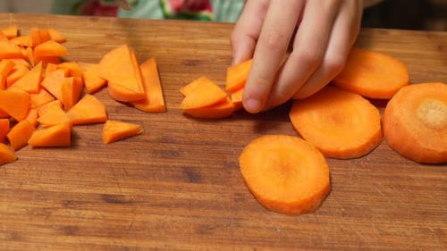 Child Slices Carrots with Knife on Cutting Board