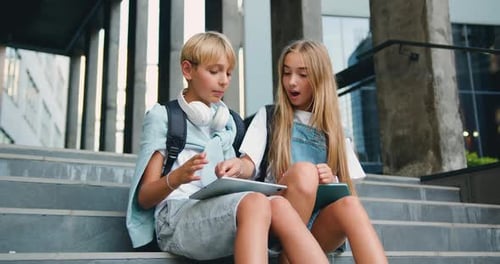 Positive teenage boy and a girl walking sittingding near school building on the stairs, having fun,