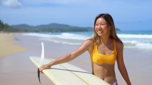 4K Asian woman holding surfboard walking to the ocean in summer sunny day.