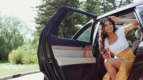Cheerful young woman in car looks at phone