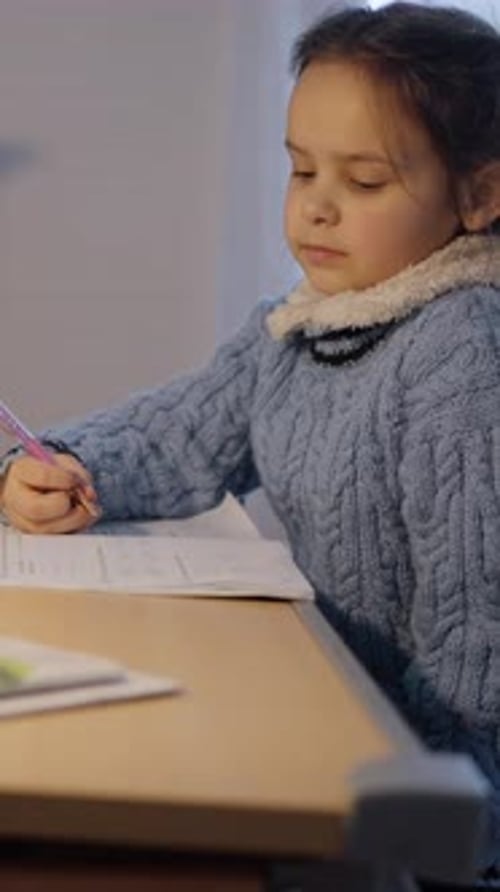 A Young Girl Engaged in Studying at Home While Wearing a Cozy Sweater for Comfort